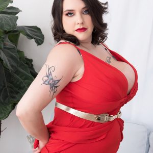 Tattooed BBW Nagini takes off a red dress while making her nude debut on a couch